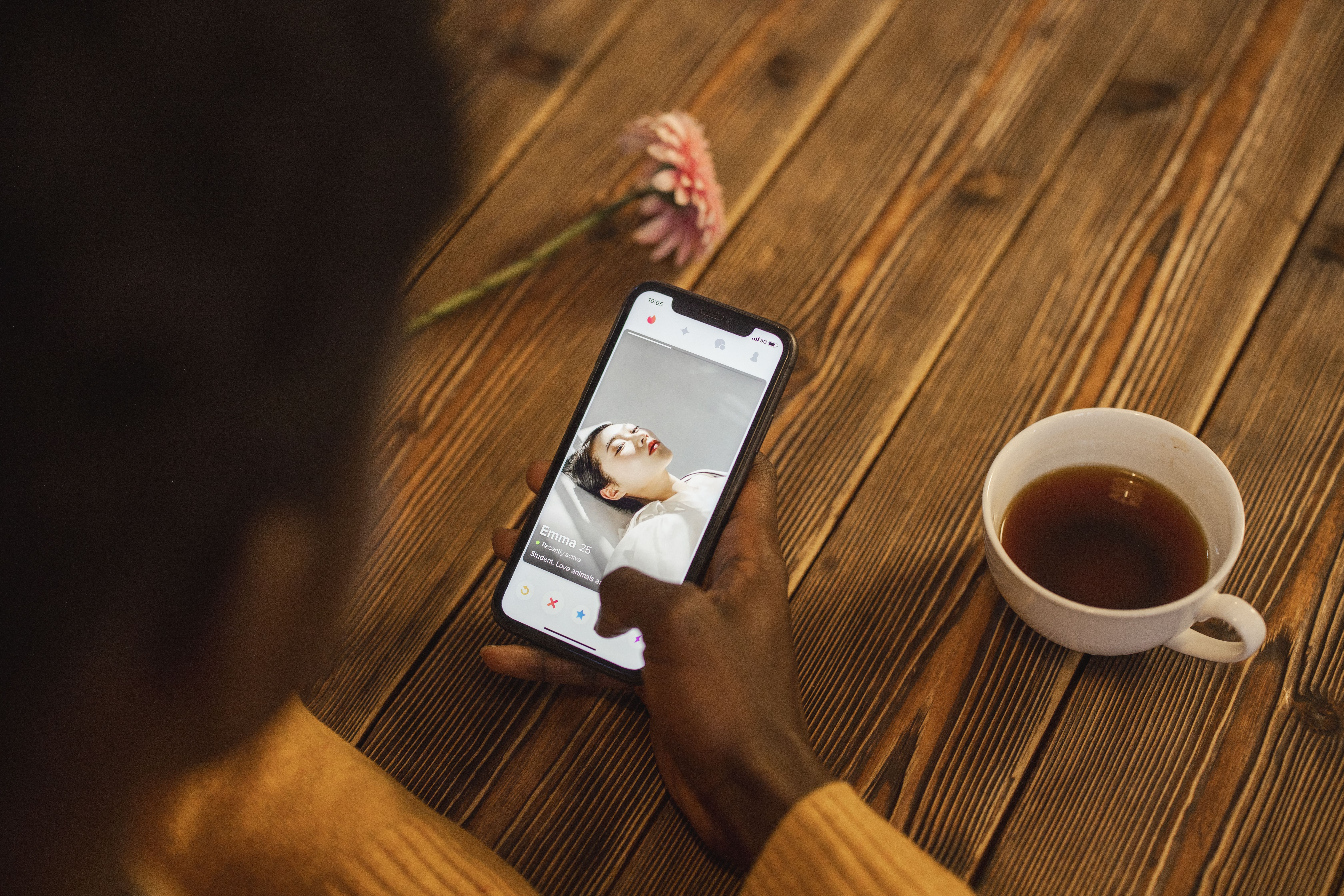 Individual swiping on a dating app on a smartphone with a cup of tea on a wooden table