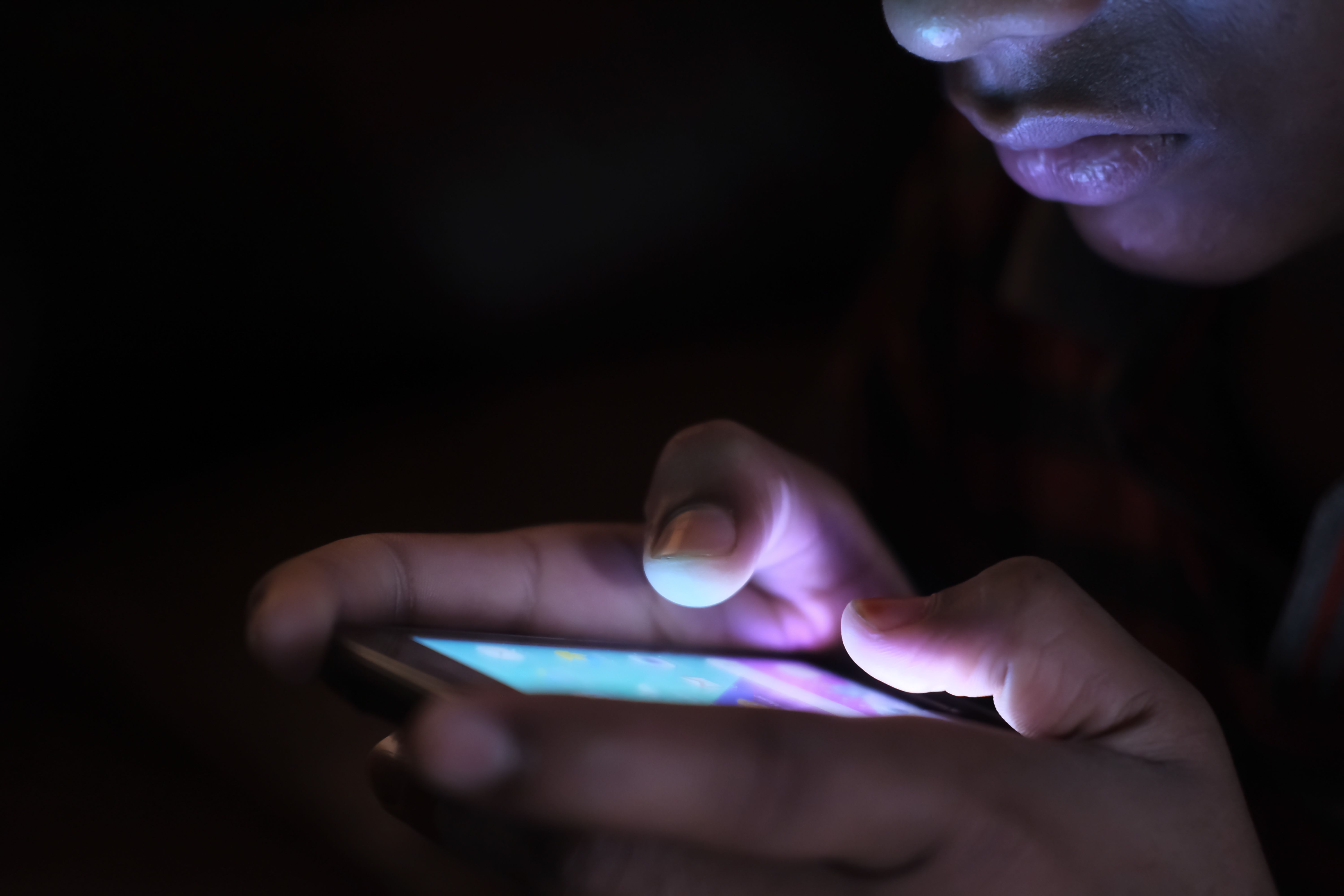 Close-up of a person holding an illuminated smartphone in the dark while texting late at night